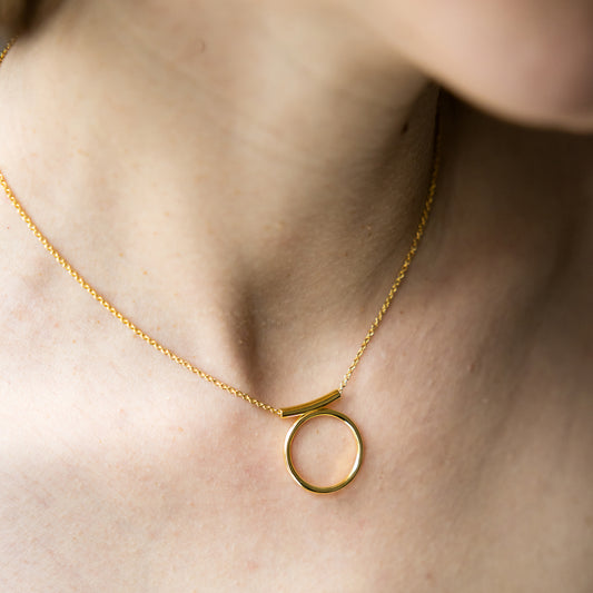 Gold necklace with a circular pendant on a person's neck