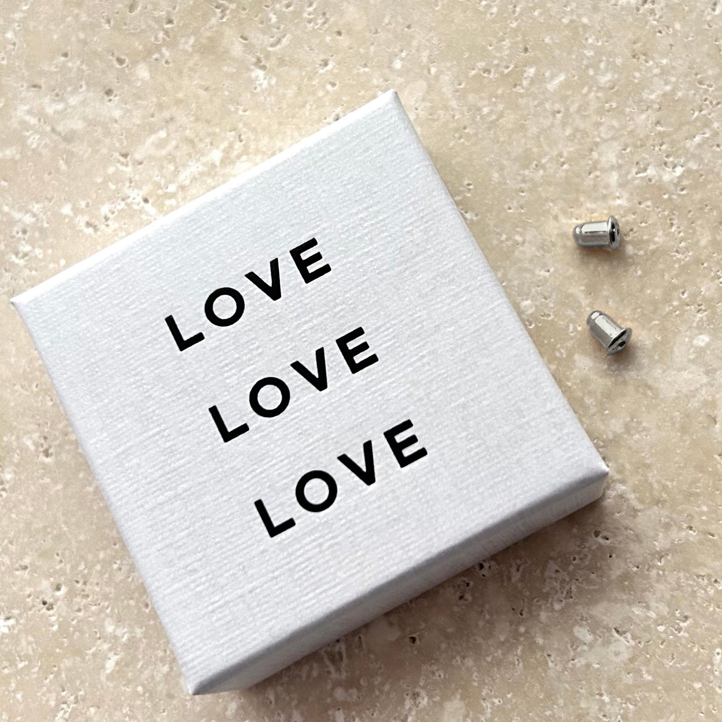Silver earring backings and white box with 'LOVE' text on a beige surface