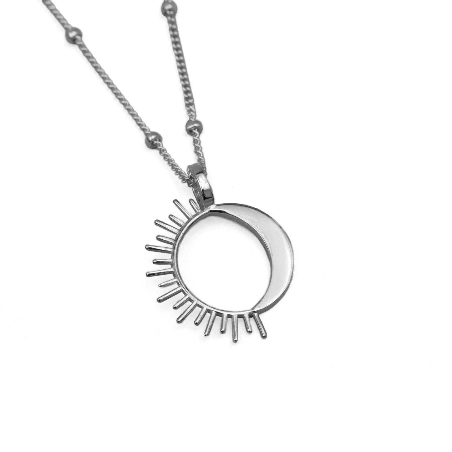 A silver-colored necklace featuring a circular pendant with a sun design on it, attached to a chain with spherical embellishments.