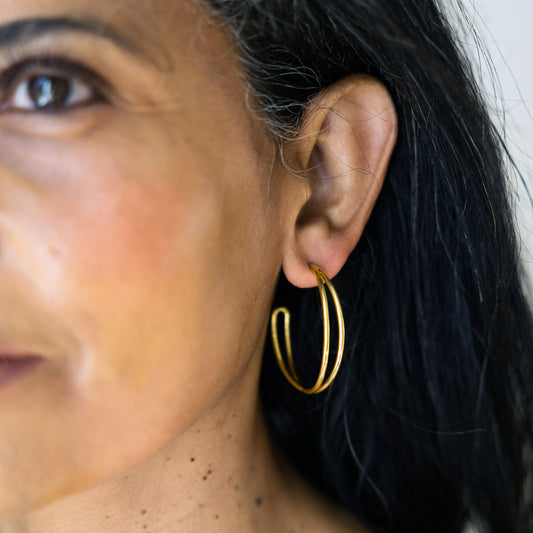 Close-up of a person wearing gold hoop earrings with a blurred background