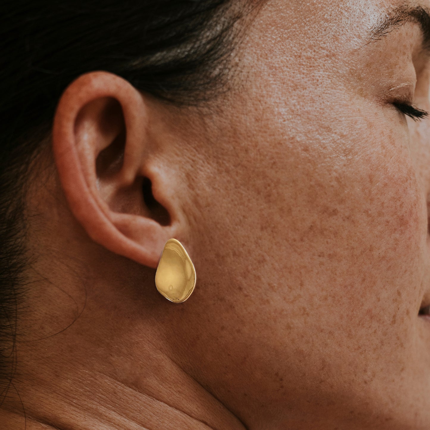 Gold flower petal earring on woman's ear
