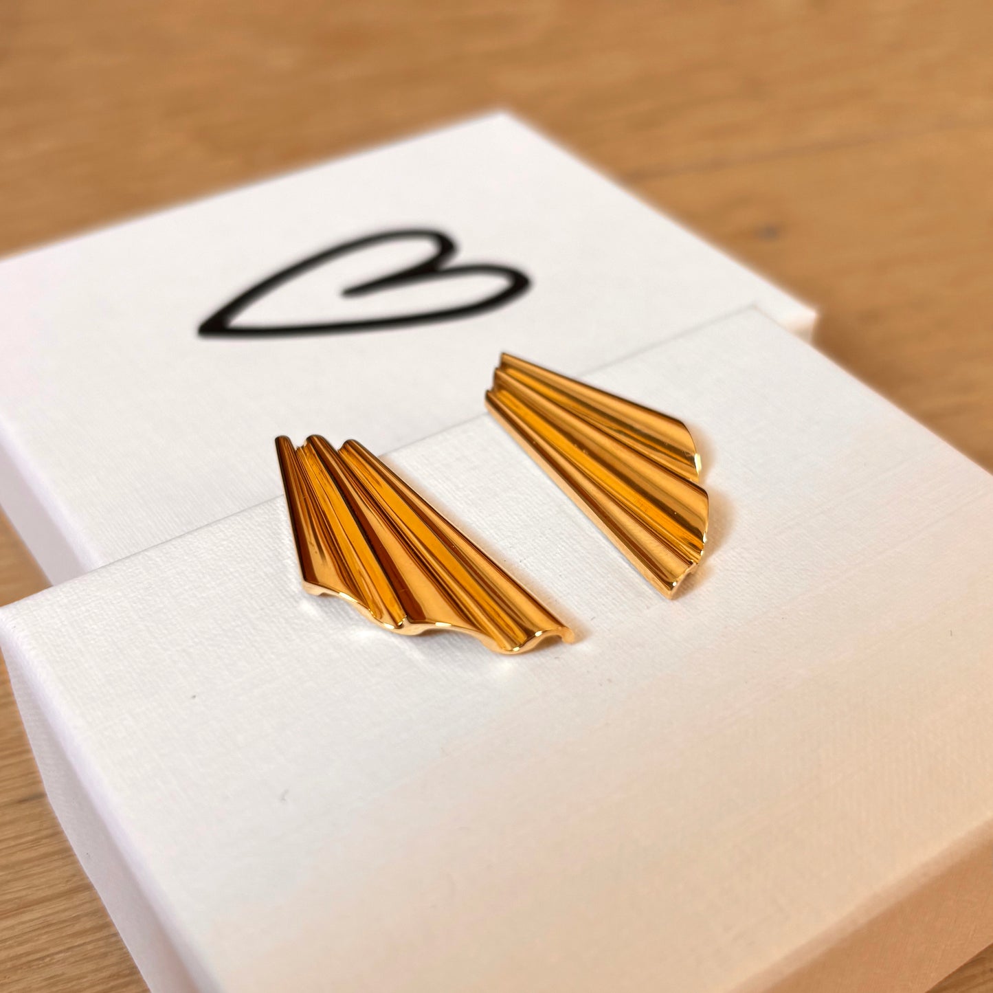 gold modern shell earrings shown laying on top of jewelry box with heart on it