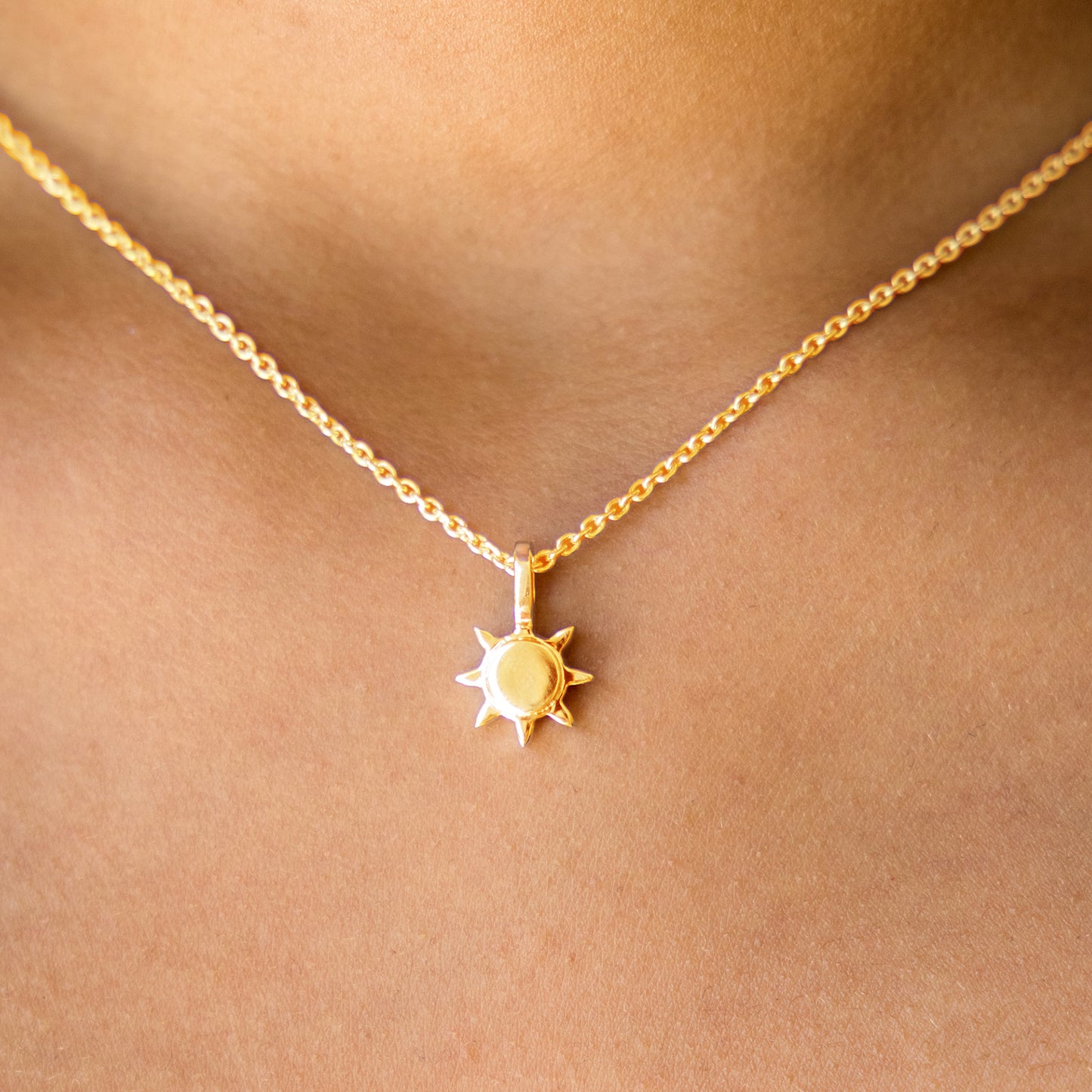 Gold necklace with a sun pendant on a person's neck