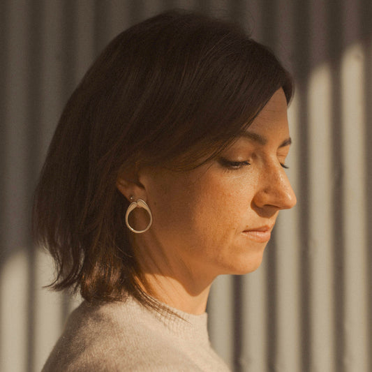 Person wearing a circular gold earring on a neutral background