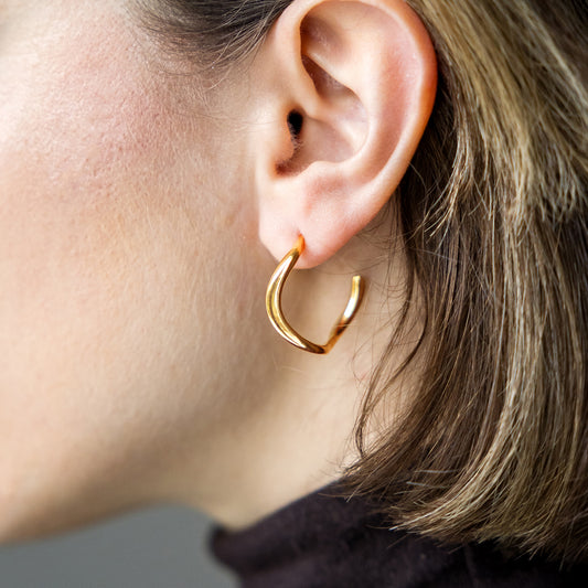 Close-up of a person wearing a gold hoop earring with a neutral background