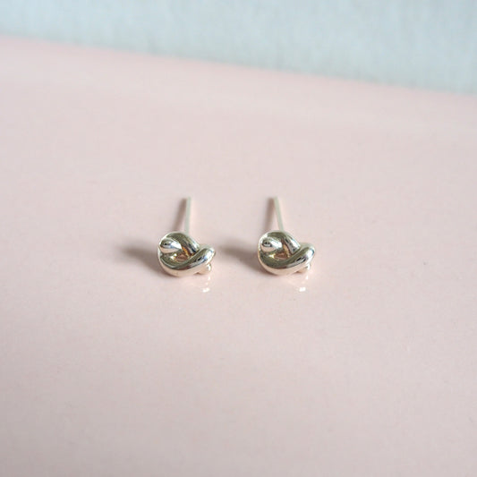 Silver knot-shaped earrings on a pink surface with a light blue background