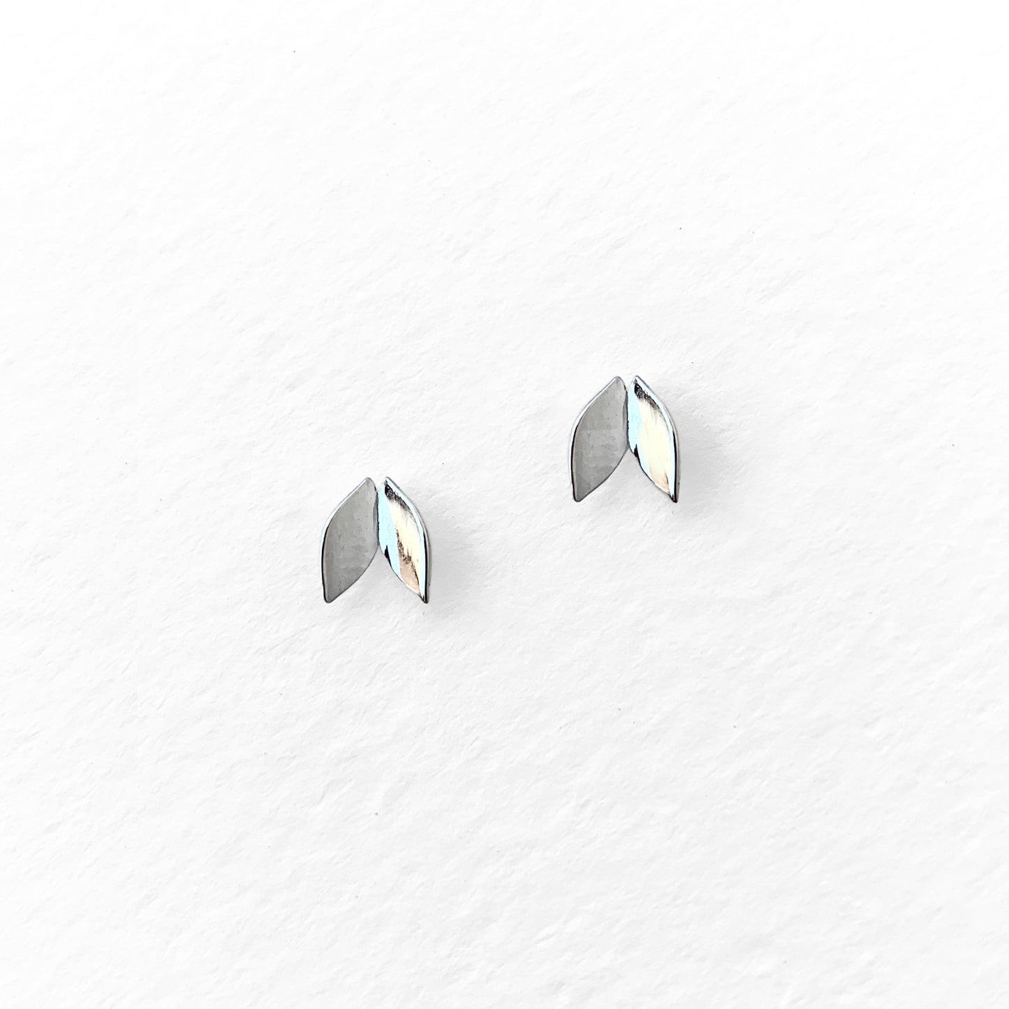 A pair of silver-colored leaf-shaped stud earrings against a white background.
