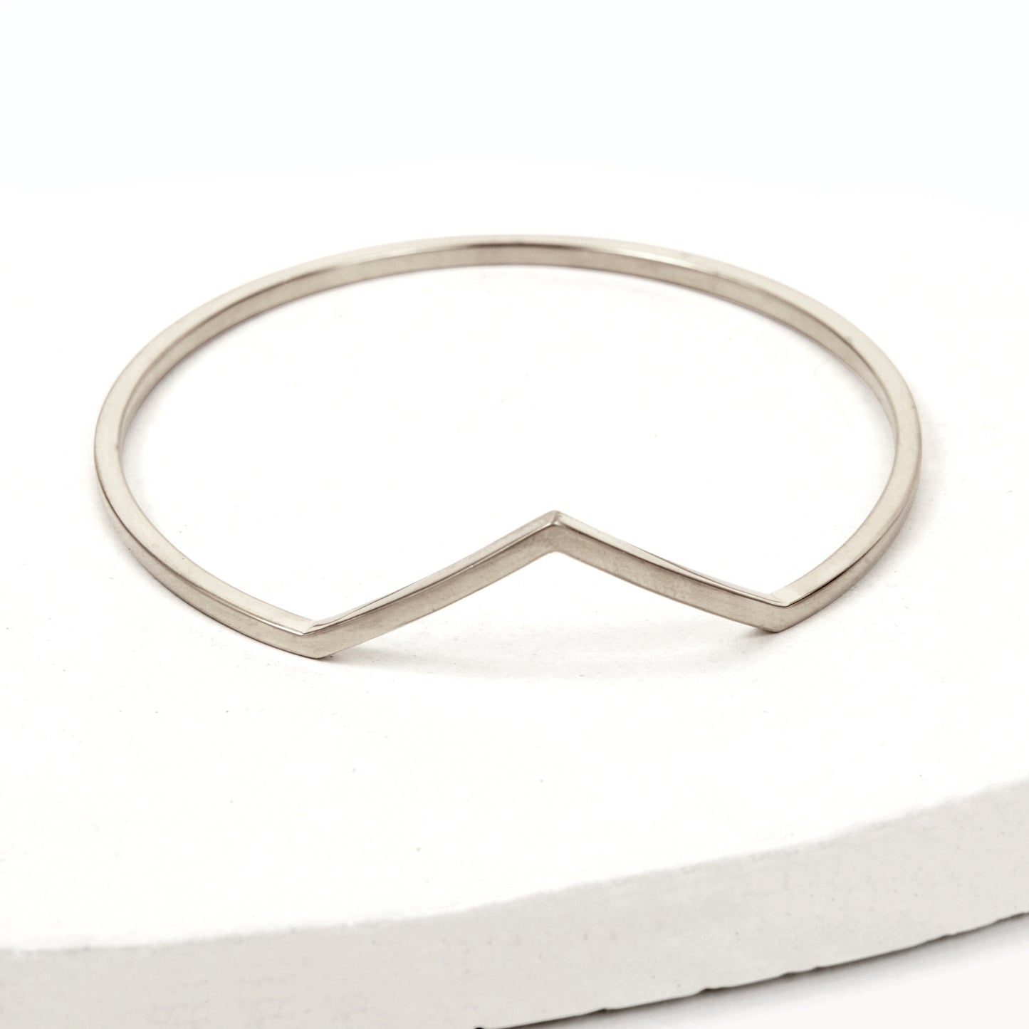 Silver bangle bracelet with triangle shaped V peak against a white background