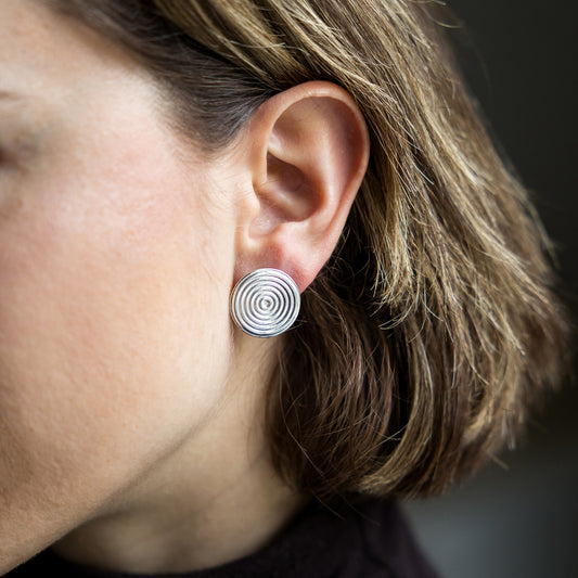 Close-up of an ear wearing a silver spiral earring with blurred background
