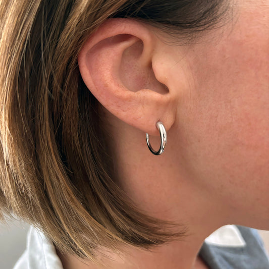 Close-up of an ear wearing a silver hoop earring with blurred background
