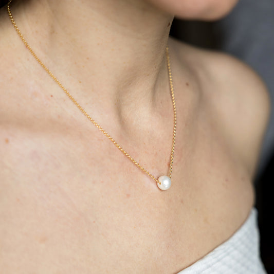 Gold necklace with a pearl pendant on a person wearing a white top.