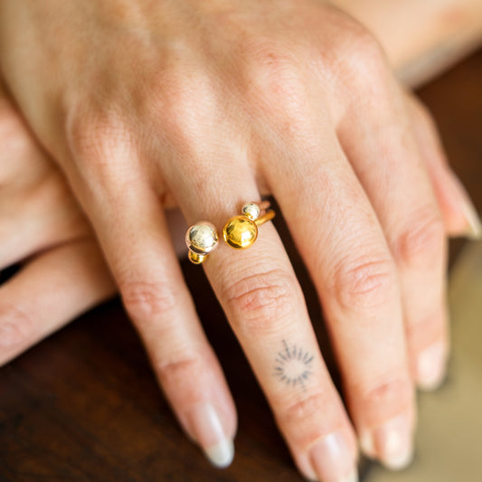 Close-up of a hand wearing a gold ring with two round stones on a wooden surface.