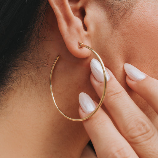 A pair of gold-colored hoop earrings with starburst designs attached to the hoops