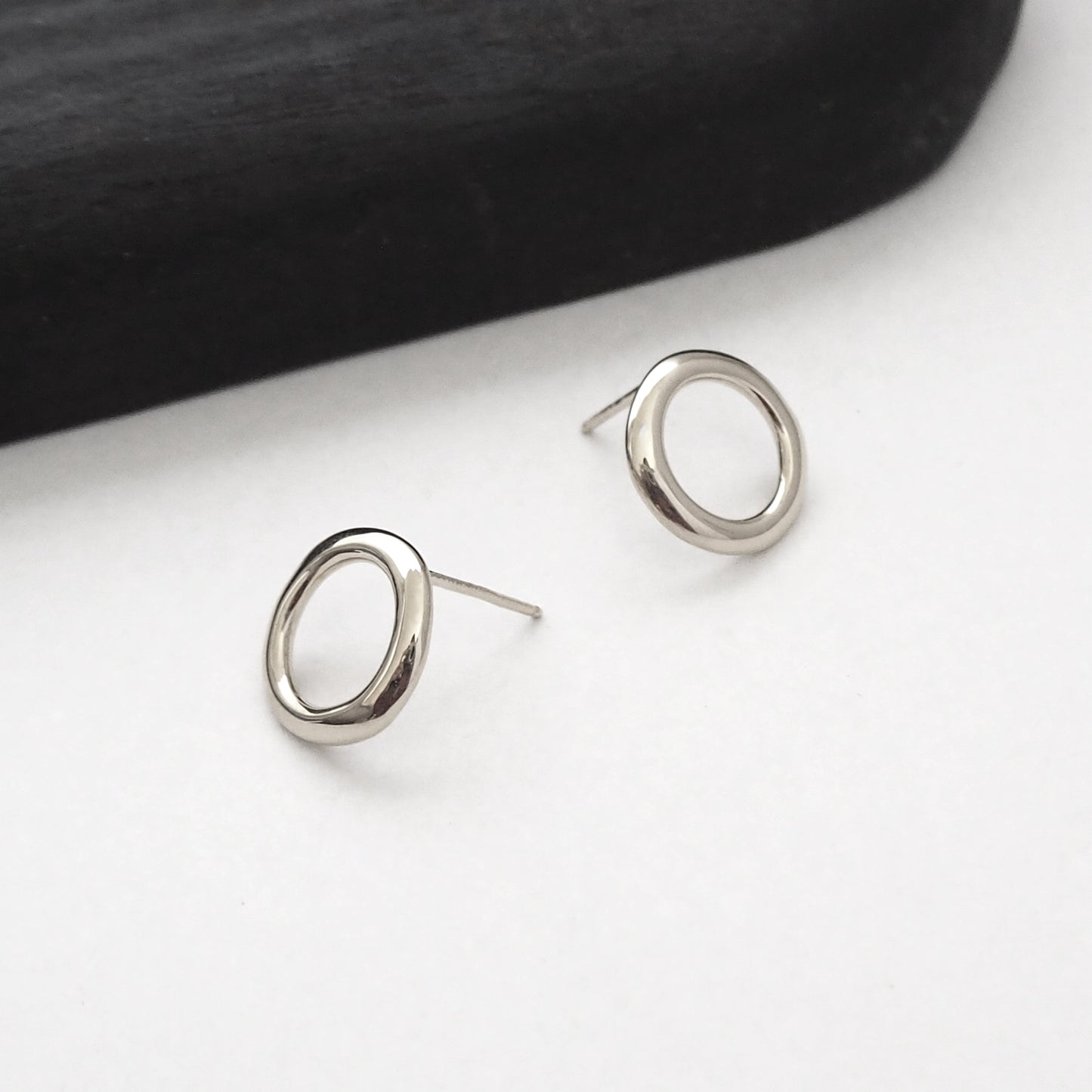 Silver circular earrings on a white surface with a black background
