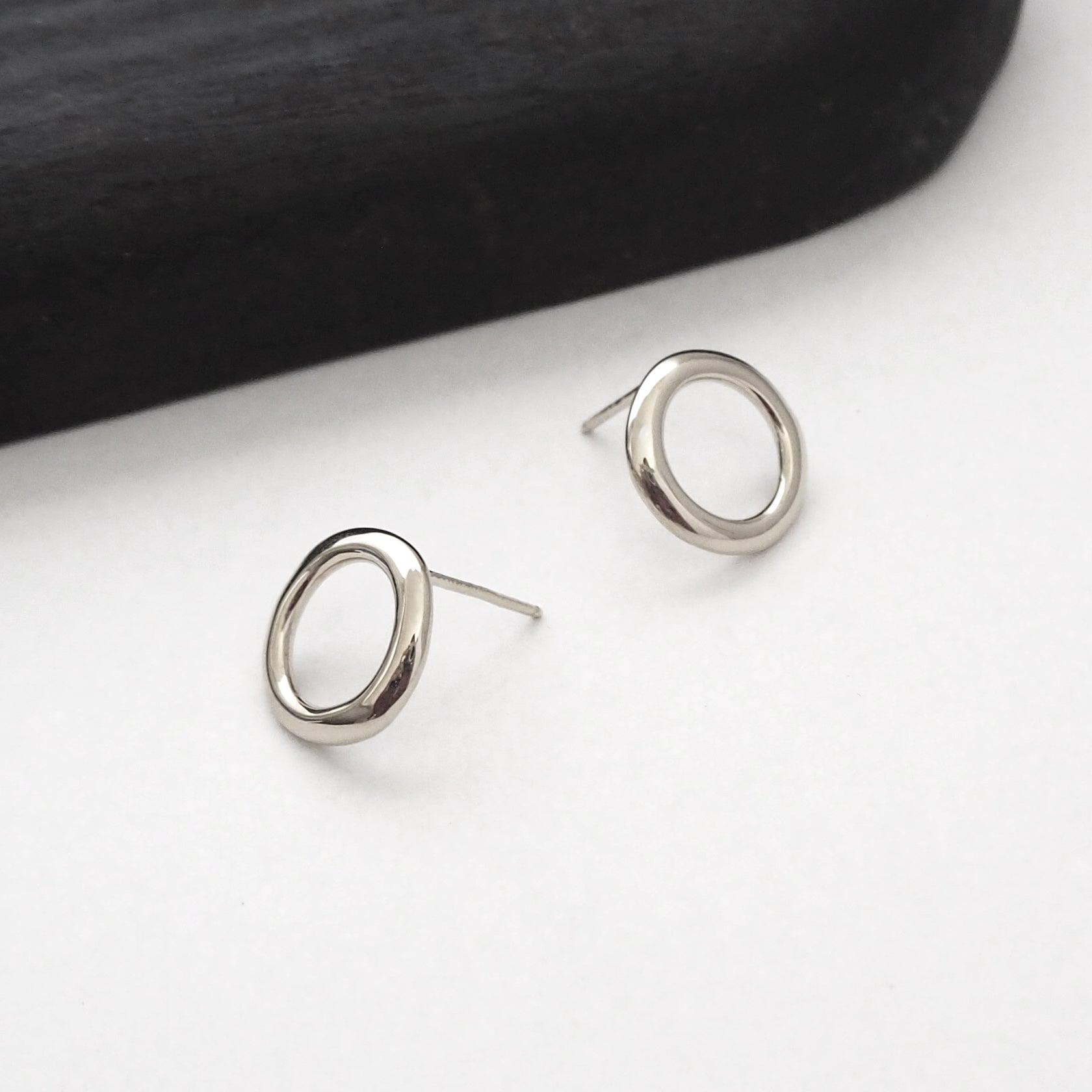Silver circular earrings on a white surface with a black background