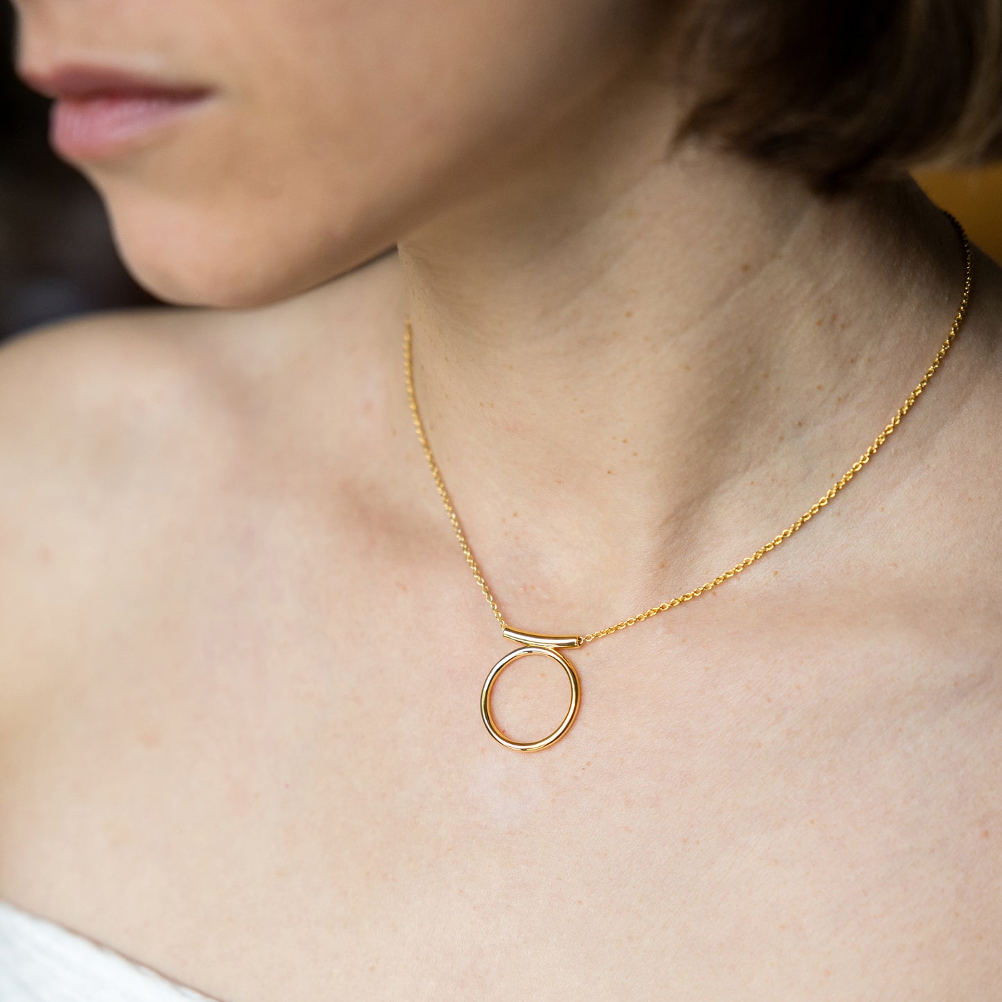 Gold necklace with a circular pendant on a person's neck