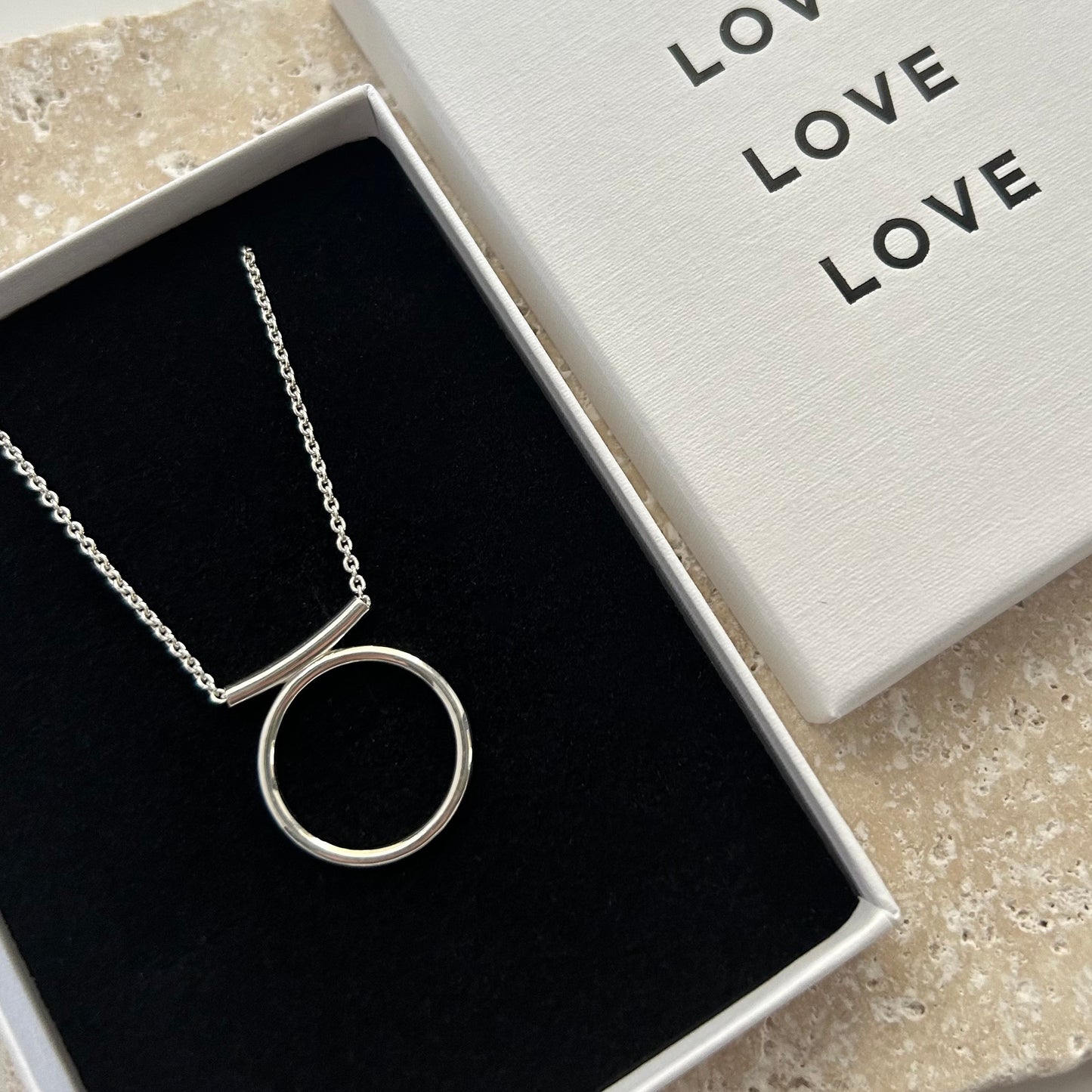 Silver necklace with a circular pendant in a box labeled 'LOVE'.