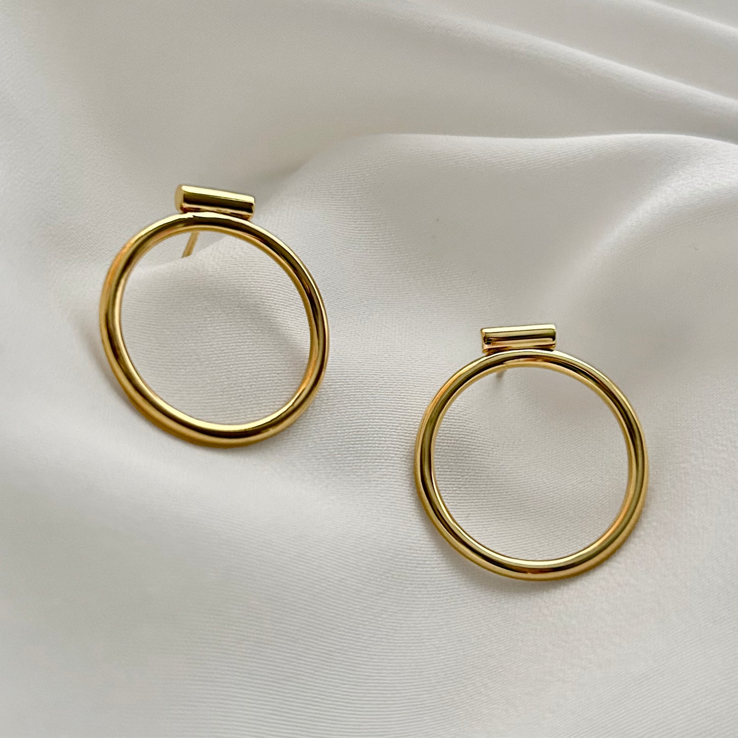 Gold hoop earrings on a white satin background