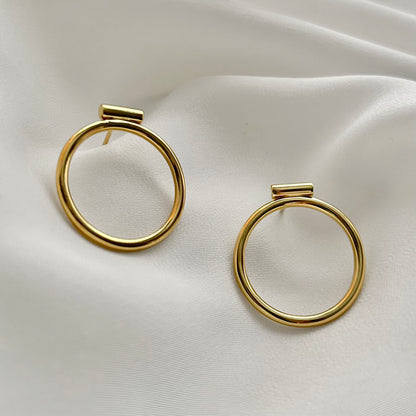 Gold hoop earrings on a white satin background