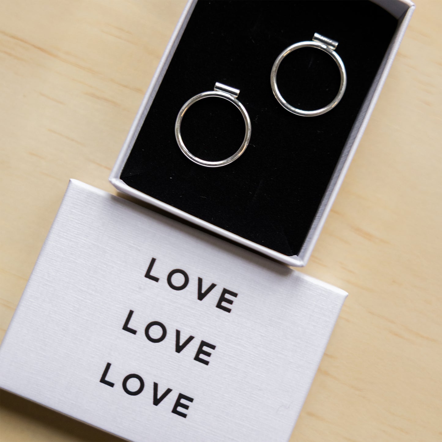 Silver hoop earrings in a box with 'LOVE' card on a wooden surface