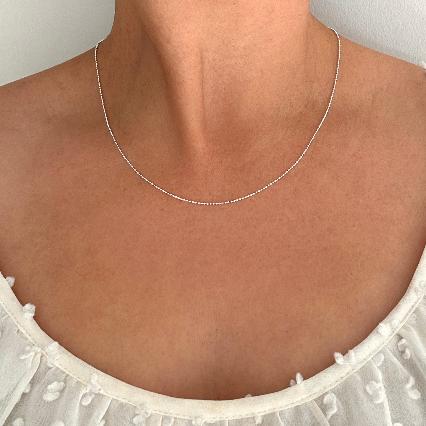 Close up of a person wearing a silver ball bead chain necklace.