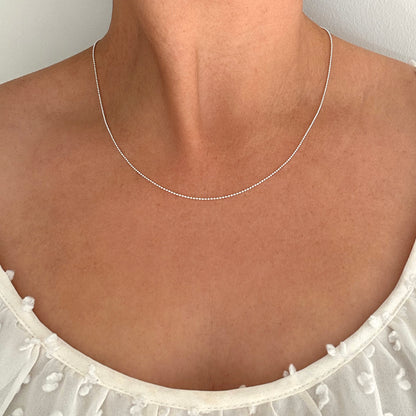 Close up of a person wearing a silver ball bead chain necklace.