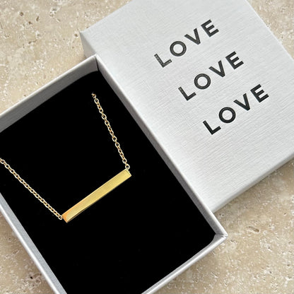 Gold necklace in an open box with 'LOVE' text on a light background