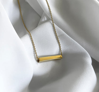 Gold necklace with a bar pendant on a white fabric background
