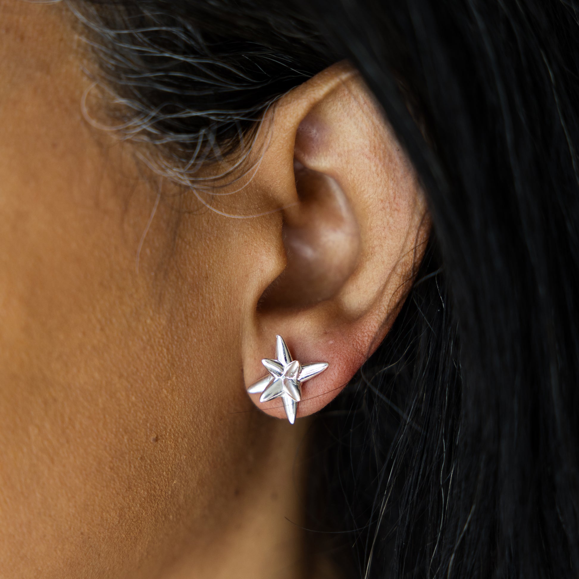 Close-up of an ear wearing a star-shaped silver earring with dark hair