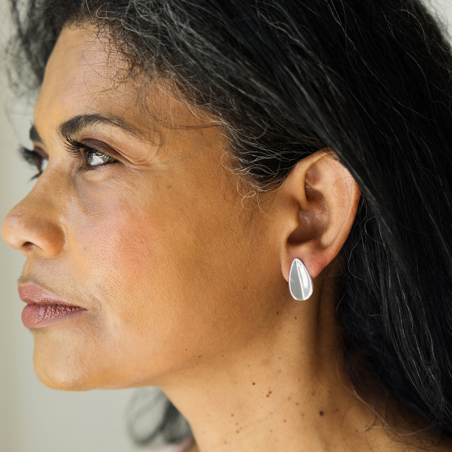 Close-up of a woman wearing a silver earring with a neutral background