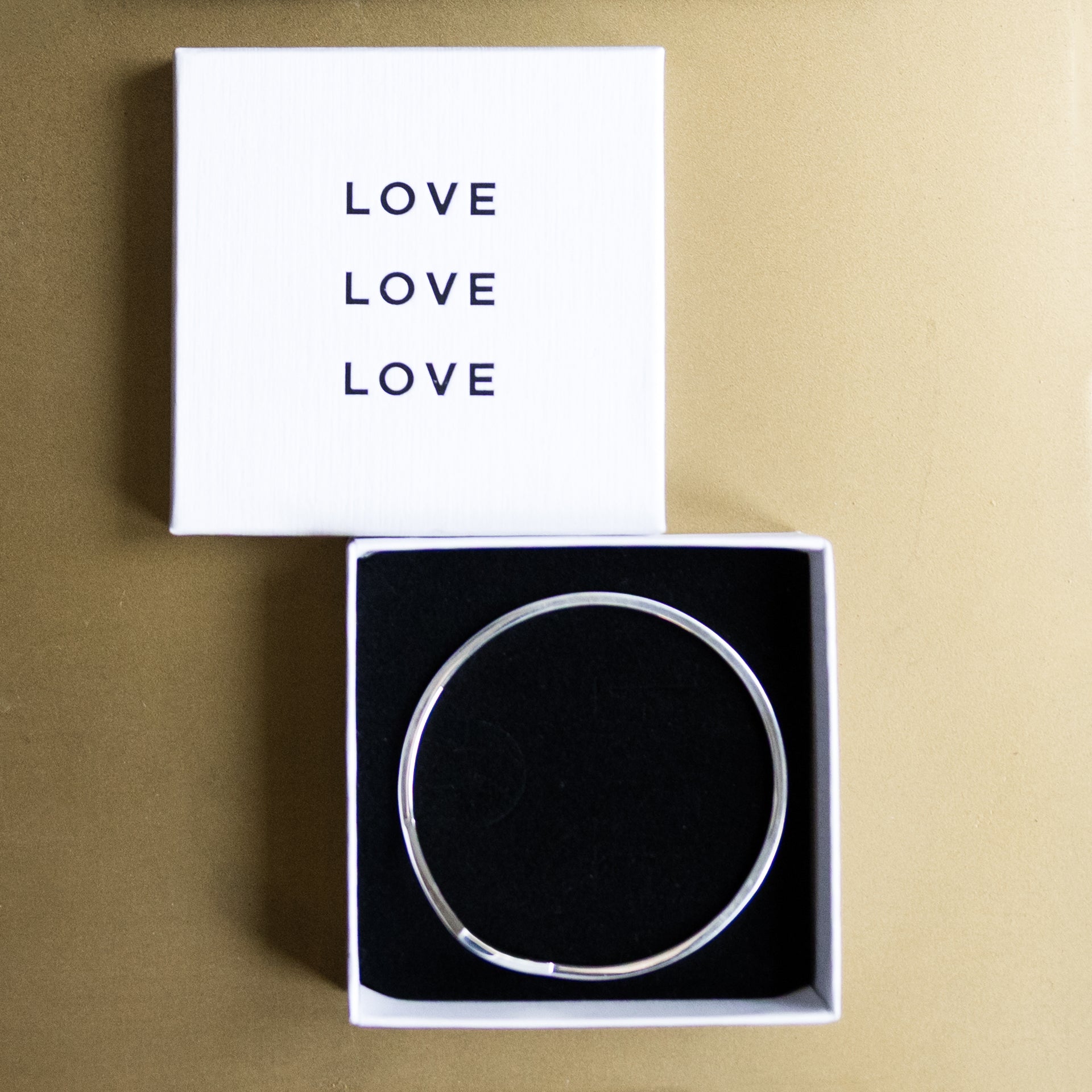 Silver bracelet in a box with 'LOVE' text on a beige background