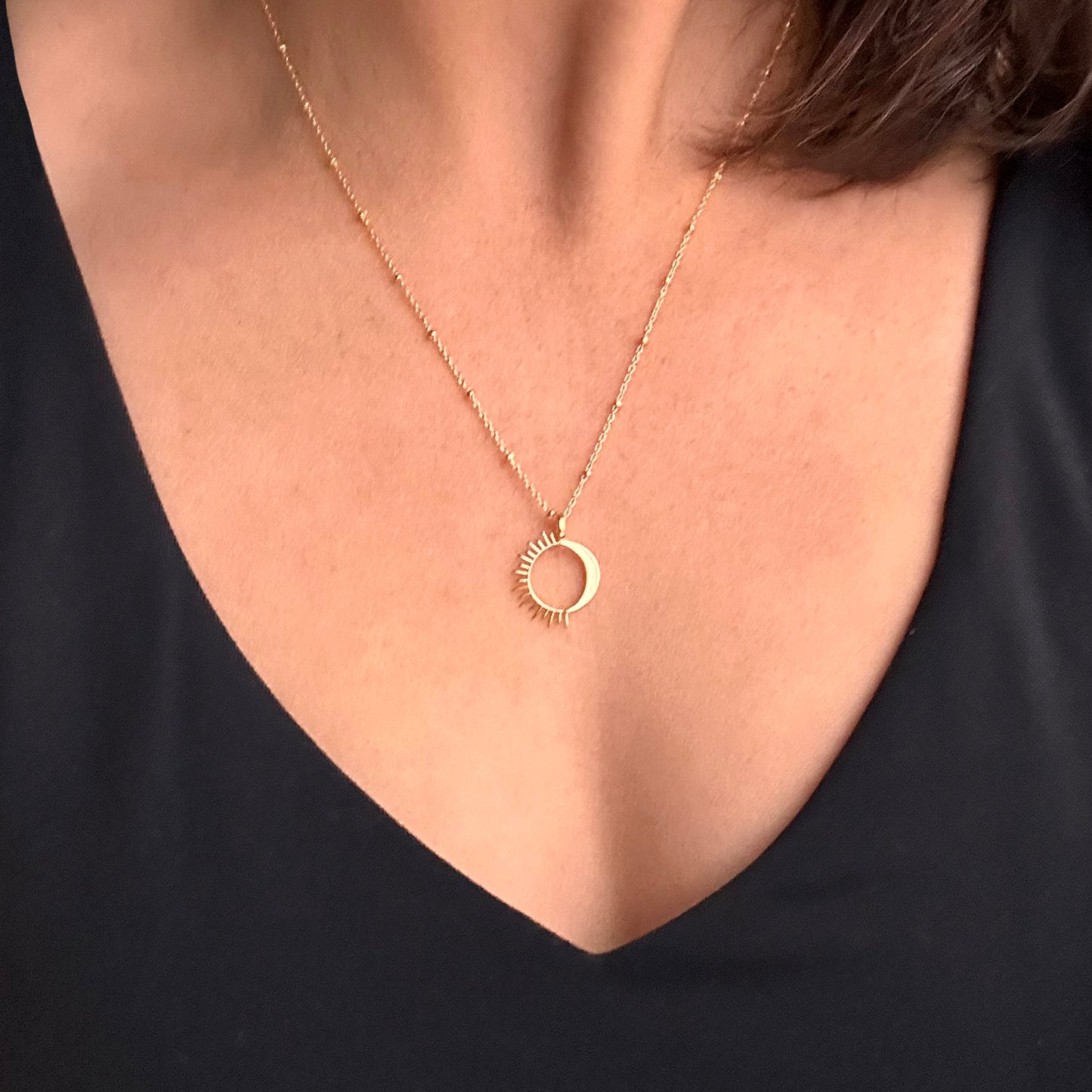 Close up of a person wearing a gold sun and moon necklace
