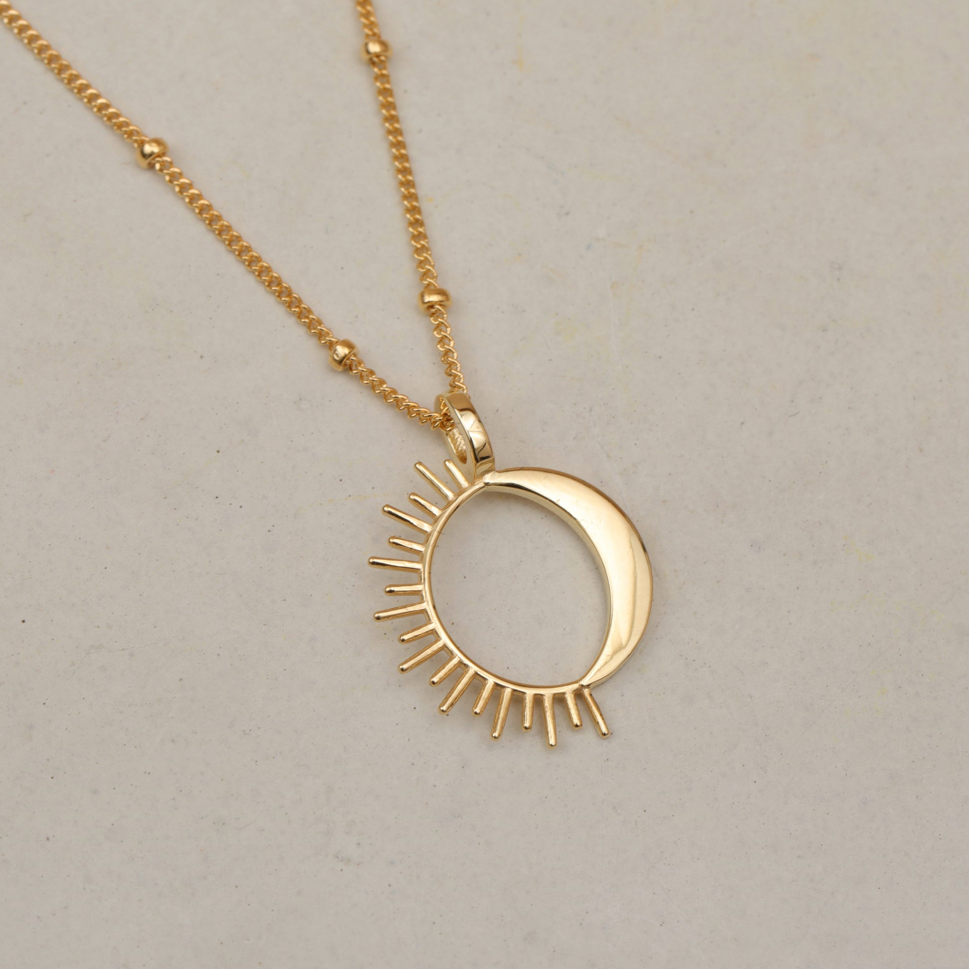 Close up of a gold sun and moon pendant necklace on a white background