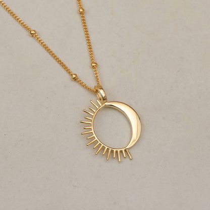Close up of a gold sun and moon pendant necklace on a white background