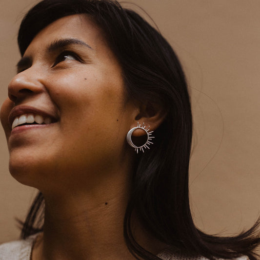 Person wearing silver sun and moon earrings on a neutral background