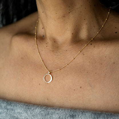 Gold necklace with a circular sun moon pendant on a person's neck