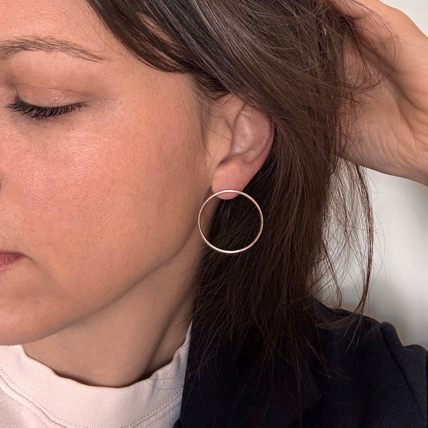 A person wearing a pair of gold-colored circular earrings.