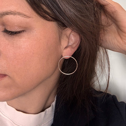 A person wearing a pair of gold-colored circular earrings.