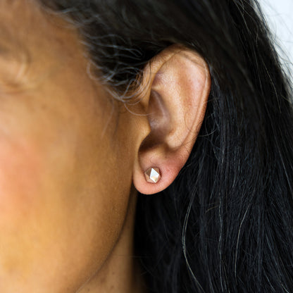 Close-up of an ear wearing a diamond-shaped earring with blurred background
