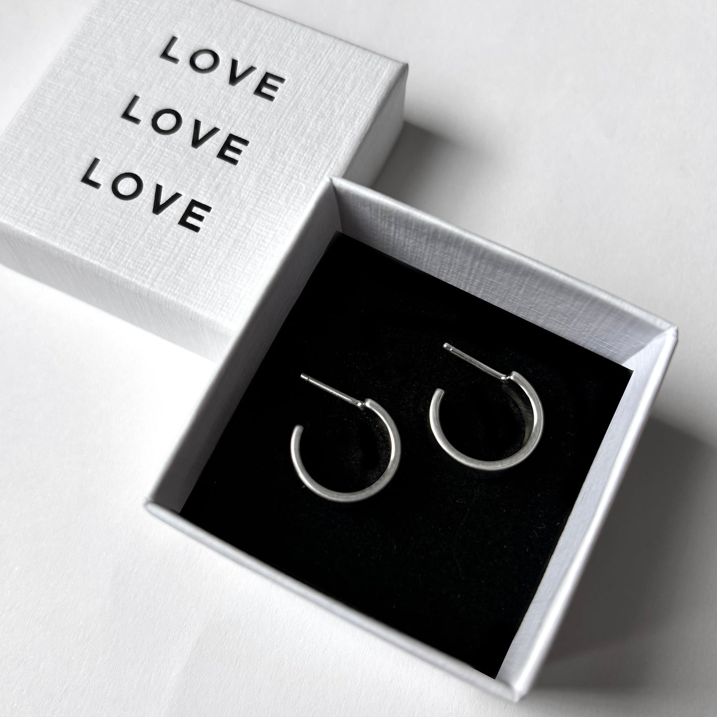 Silver hoop earrings in a box with 'LOVE' text on a white background
