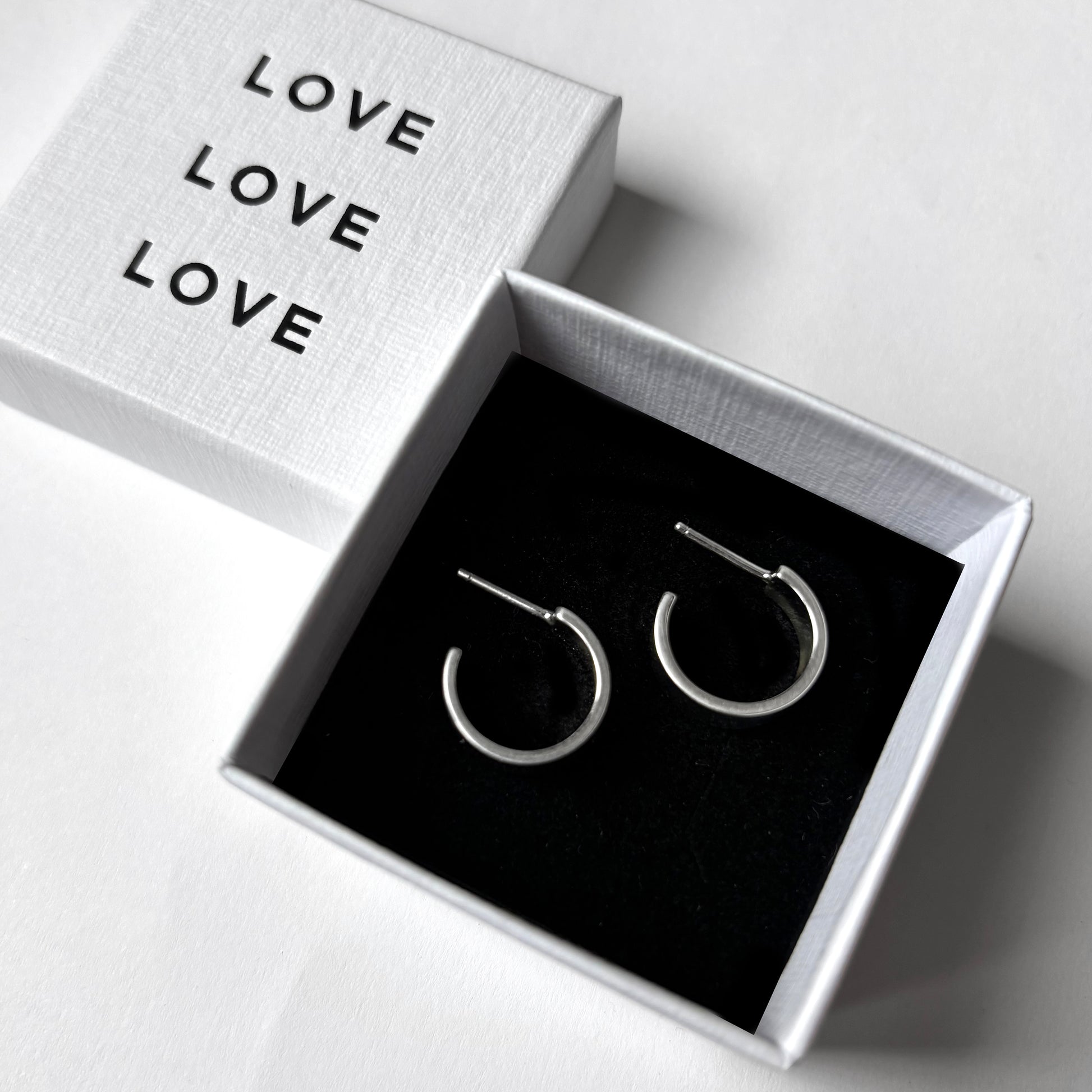 Silver hoop earrings in a box with 'LOVE' text on a white background