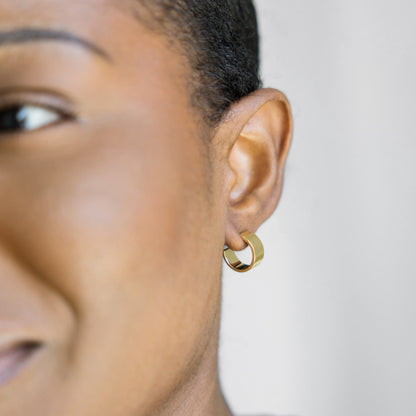 Close-up of a person wearing a gold hoop earring against a neutral background