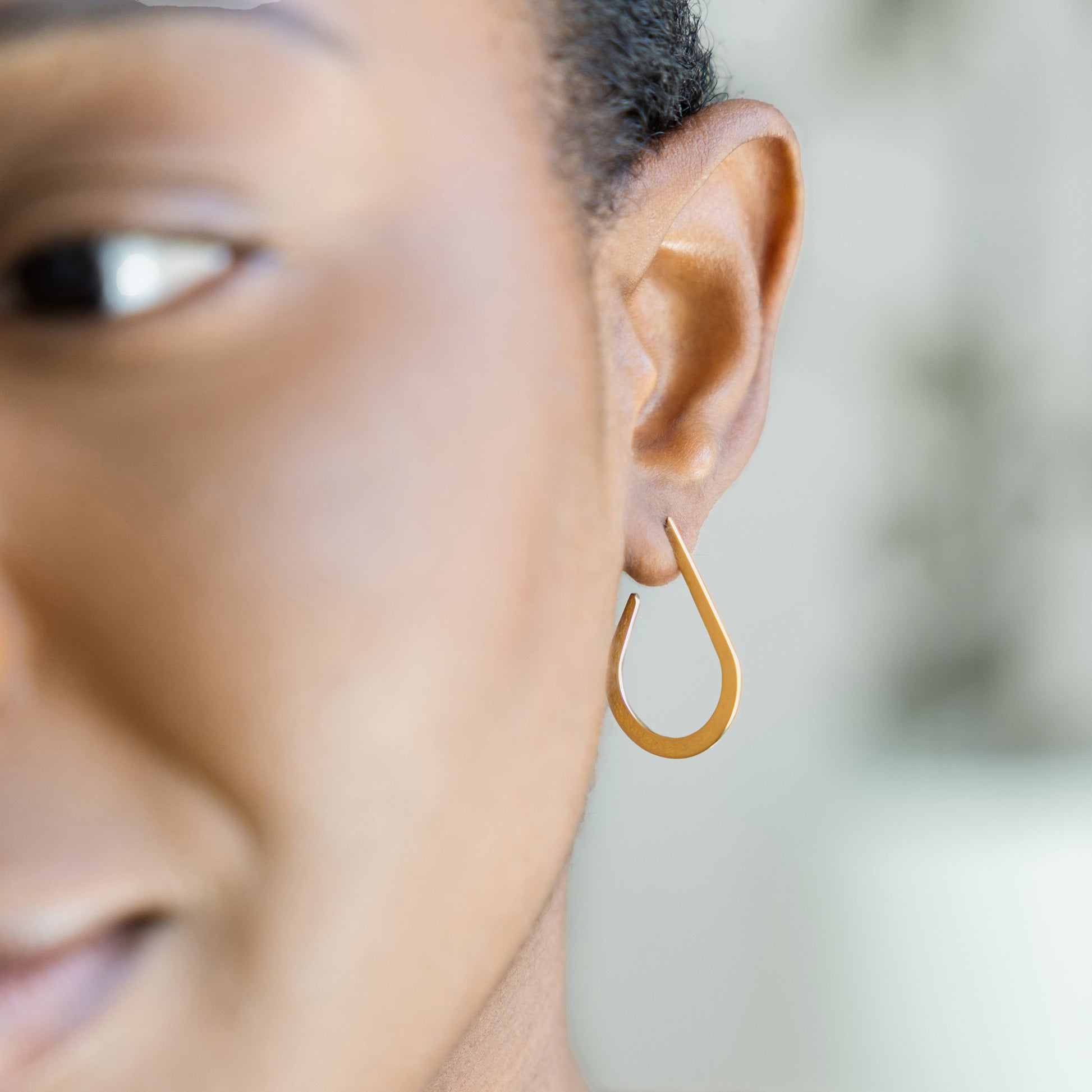 Close-up of a person wearing a gold hoop earring with a blurred background