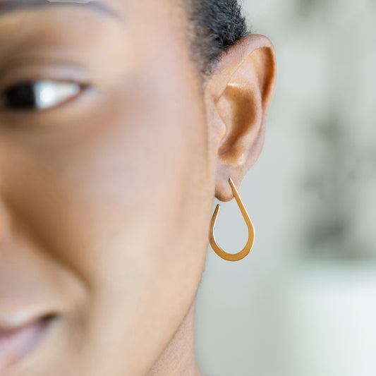 Close-up of a person wearing a gold hoop earring with a blurred background