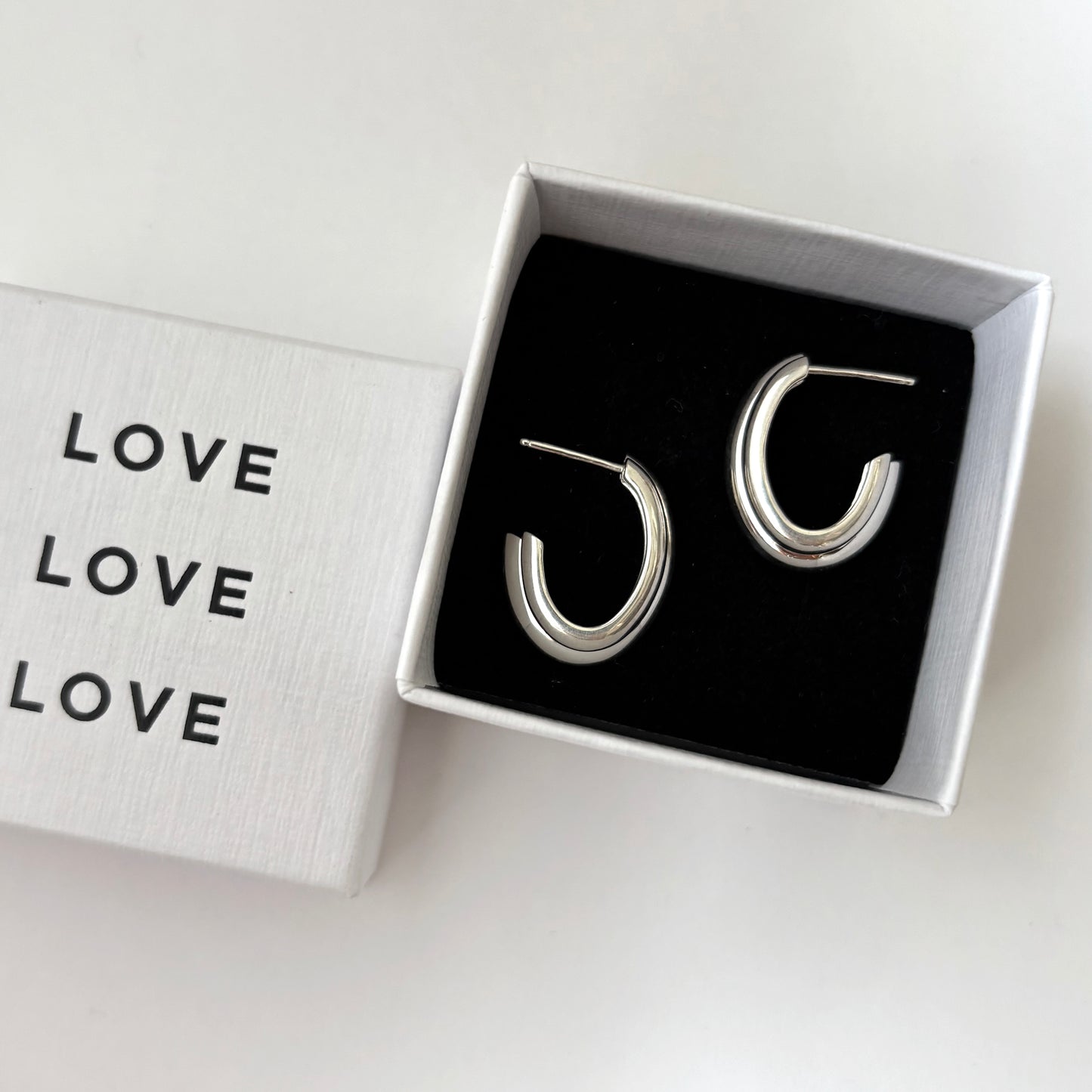 Silver hoop earrings in a box with 'LOVE' text on a white background