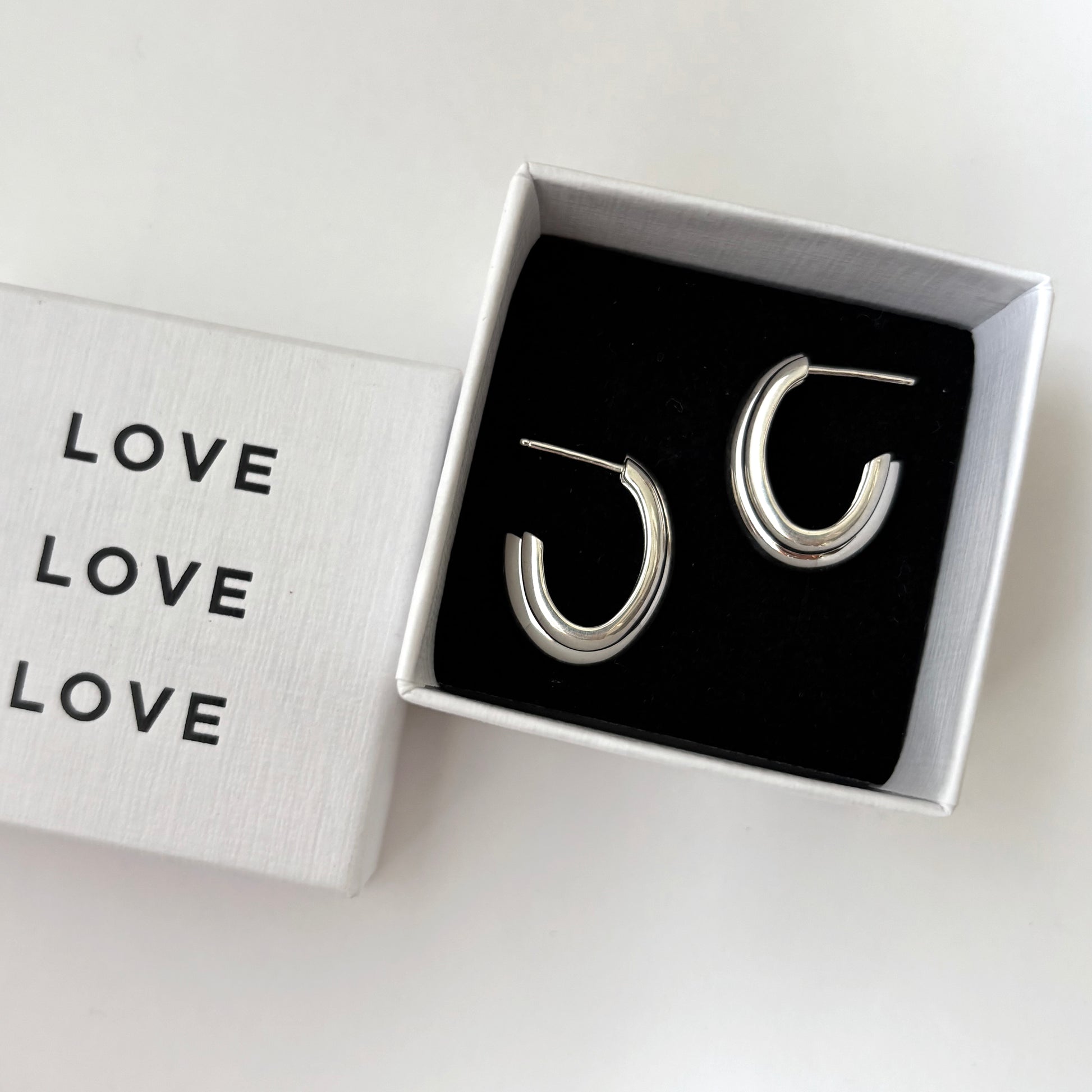 Silver hoop earrings in a box with 'LOVE' text on a white background