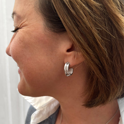 Close-up of a woman wearing silver hoop earrings with a neutral background