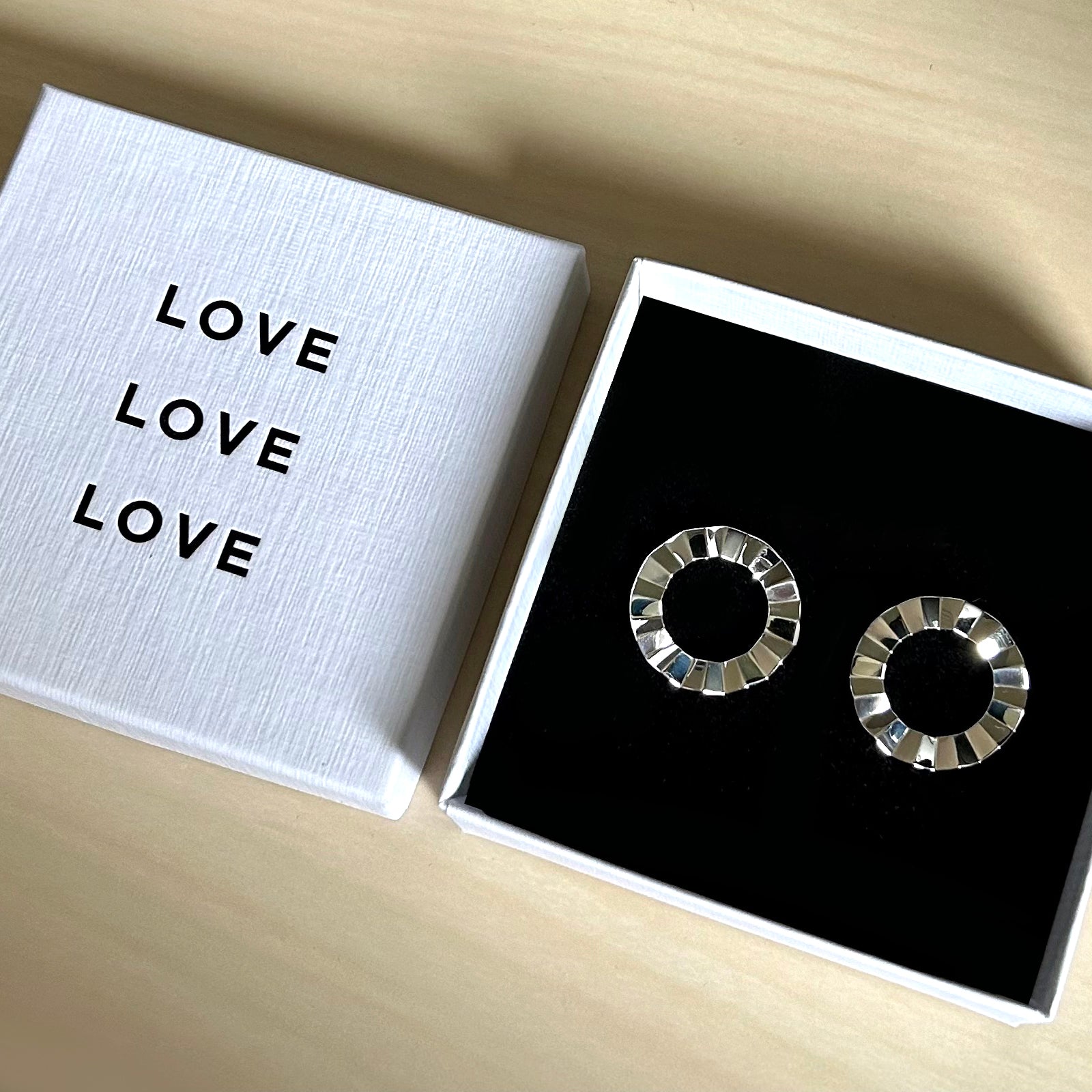 Silver hoop earrings in a box with 'LOVE' text on a wooden surface