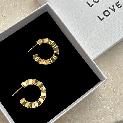 Gold hoop earrings in a box with 'LOVE' text on a light surface