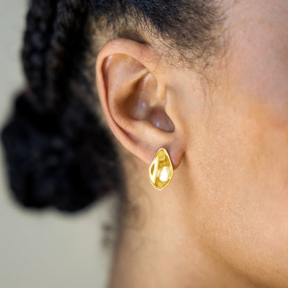 Gold petal earring worn by a person with a blurred background